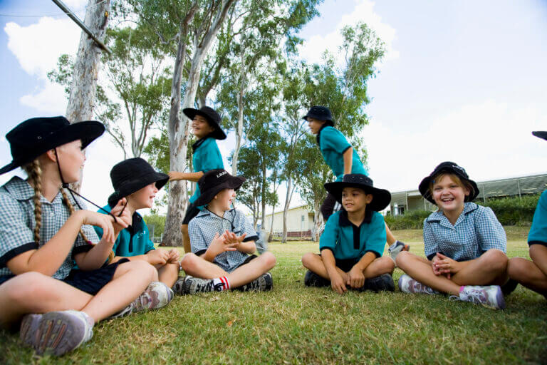 primary school children sitting on grass wearing hats to protect themselves from the sun